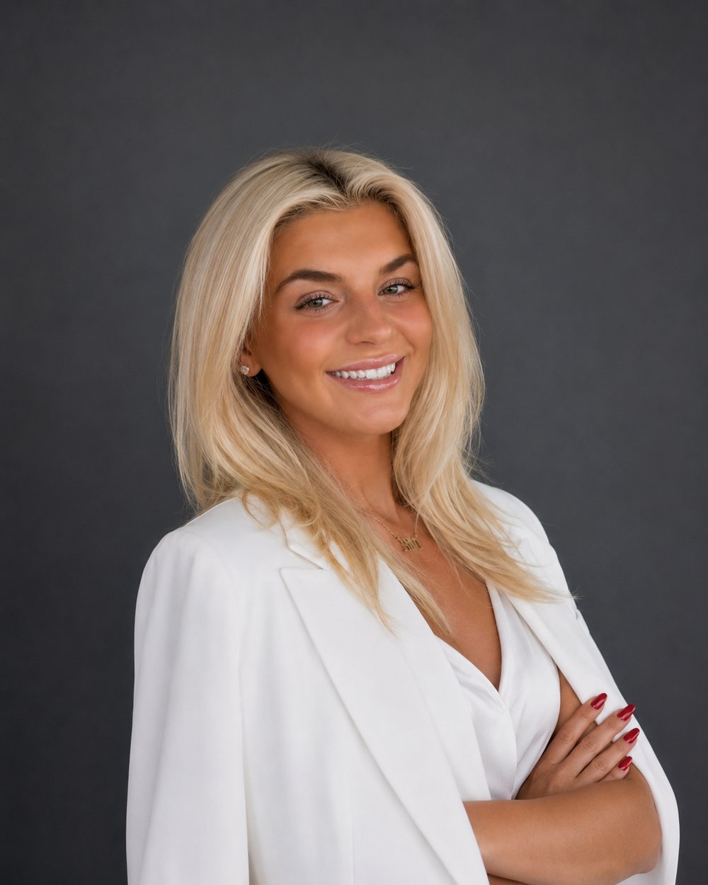 Emily McElligott smiling, wearing a white blazer, arms crossed, against a charcoal backdrop